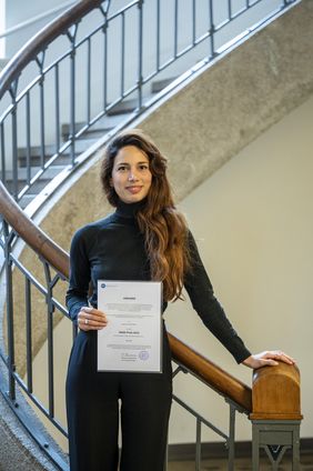 Foto: Thomas Müller / Bauhaus-Universität Weimar Betül Peker auf der Treppe im Foyer des Hauptgebäudes, sie hält ihre Auszeichnung vor sich.
