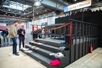 Exhibition view of »Ein Messestand für Leipzig«: visitors stand in front of the Faculty of Art and Design’s trade fair stand, staged as an underground station entrance. Publications and textiles from the university are displayed on the steps.
