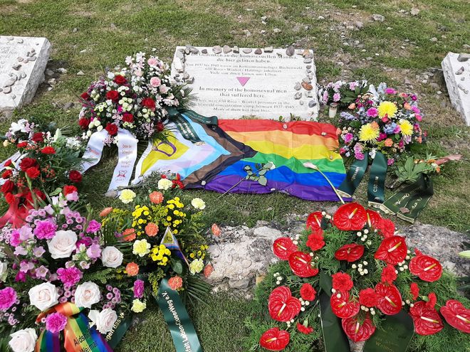 The photo shows various flower arrangements at the memorial stone for the homosexual men imprisoned and murdered by the Nazis in the Buchenwald and Mittelbau-Dora concentration camps. The memorial plaque bears the inscription (in German and English): »In memory of the homosexual men that suffered here / There were 650 Rosa Winkel prisoners in the Buchenwald concentration camp between 1937 – 1945. Many of them lost their lives«.