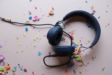 The symbolic image shows a pair of headphones lying on a white table. There is colorful confetti all around.