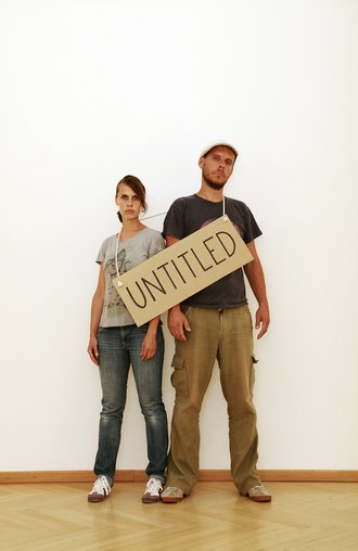 Photograph of the artist duo with a cardboard sign that reads »untitled«