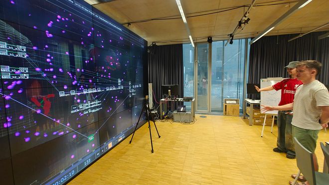 Zwei Studierende testen eine interaktive Anwendung vor der LED-Wand des Performance Platform. Bewegungen werden in Echtzeit in digitale Partikel und grafische Effekte übersetzt.