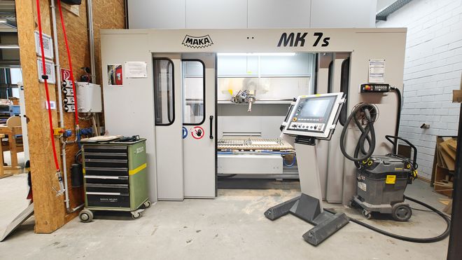 Große CNC-Fräsmaschine des Typs MK 7s in einer Werkhalle. Vor der Maschine steht ein separates Bedienpult mit Bildschirm; daneben sind Werkzeugwagen und Absauganlage zu sehen.