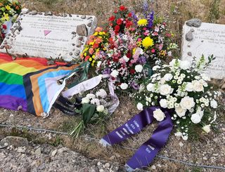 Das Foto zeigt verschiedene Blumengestecke am Gedenkstein für die homosexuellen Männer, die von den Nazis in den Konzentrationslagern Buchenwald und Mittelbau-Dora inhaftiert und ermordet wurden. Die Gedenktafel trägt die Inschrift (auf Deutsch und Englisch): »Im Gedenken an die homosexuellen Männer, die hier gelitten haben / Von 1937 bis 1945 waren im Konzentrationslager Buchenwald 650 Rosa-Winkel-Häftlinge inhaftiert. Viele von ihnen kamen ums Leben«.