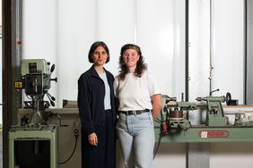 Mara Trübenbach und Mira Müller stehen in einer Werkstatt vor einer Maschine.