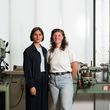 Mara Trübenbach und Mira Müller stehen in einer Werkstatt vor einer Maschine.