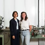 Mara Trübenbach und Mira Müller stehen in einer Werkstatt vor einer Maschine.