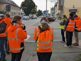 Personen in Warnkleidung stehen an einer Straße
