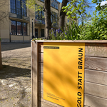 »Gold statt Braun«-Plakat vor der M18 mit Blick auf das Hauptgebäude der Bauhaus-Universität Weimar