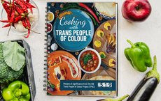 Das Bild zeigt das Kochbuch "Cooking with Trans People of Colour", umgeben von buntem Gemüse.