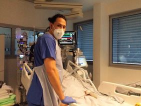 Simon Surjansenatna am Bett eines Intensivpatienten, im Hintergrund sind Monitore zu sehen. 