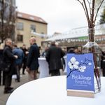 Lila Karte auf der Frühlingsempfang zum Semesterauftakt steht, dahinter stehen Menschen und unterhalten sich 