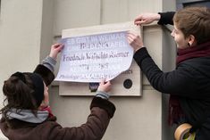 Larissa Barth (rechts) und ihre Partnerin (links) verhängen die Gedenktafel für Goethes Sekretär, Friedrich Wilhelm Riemer, in Weimars Amalienstraße. Das Plakat, mit dem sie Riemers Gedenktafel verdecken, trägt die Aufschrift: Es gibt in Weimar eine Gedenktafel für Goethes Sekretär, aber keine für Anna Amalia. 