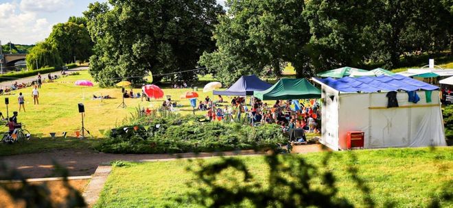 Scene from the radio play summer: Meadow with tents, colourful umbrellas and people; Photo: Tino Pfund