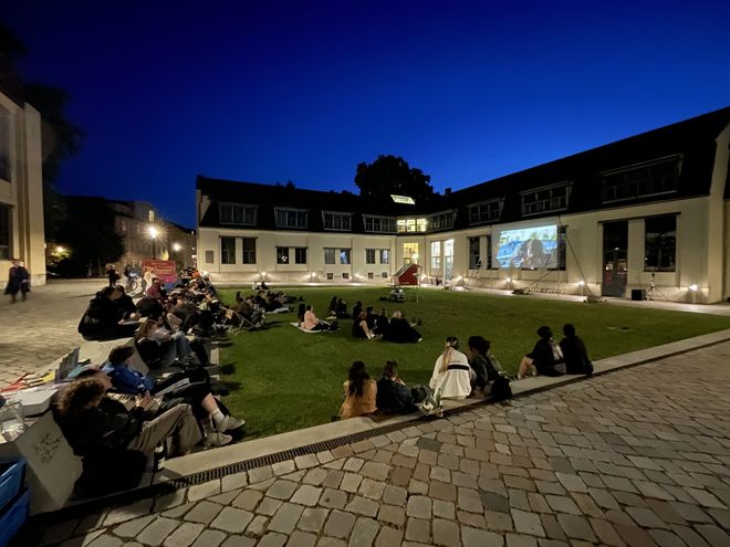 Photo taken during the screening. It shows the guests on the lawn in front of the Van de Velde Building and the screen.