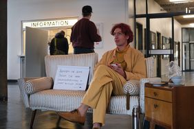Filmstill: Jakob Margit sitz im Wartebereich einer Behörde. Nebeb ihm ein Schild mit der Aufschrift »Kennen Sie iene Person, die ihren Geschlechtseintrag in »divers« ändern möchte?«; ein Richtungspfeil zweigt auf Jakob Margit