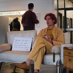 Filmstill: Jakob Margit sitz im Wartebereich einer Behörde. Nebeb ihm ein Schild mit der Aufschrift »Kennen Sie iene Person, die ihren Geschlechtseintrag in »divers« ändern möchte?«; ein Richtungspfeil zweigt auf Jakob Margit