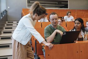 Student im Hörsaal bekommt etwas von der Dozentin erklärt. 