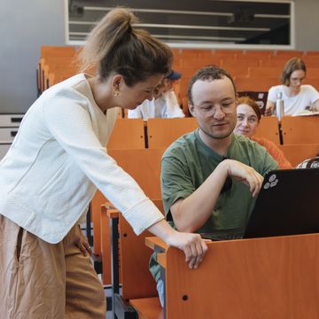 Student im Hörsaal bekommt etwas von der Dozentin erklärt. 