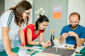 Three people tinker with a project.