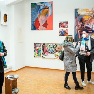 Visitors at the Winterwerkschau 2022 in the space of the Fine Arts Department, people stand in front of colourful paintings.