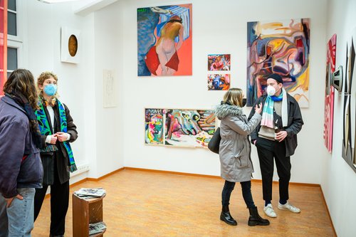 Besucher*innen auf der Winterwerkschau 2022 in den Räumlichkeiten der Freien Kunst, Menschen stehen vor farbenfrohen Gemälden