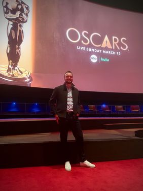 Guido Wolter beim 98. Academy Awards VFX Bake-Off in Los Angeles Person steht auf einem roten Teppich in einem großen Kinosaal. Im Hintergrund zeigt eine Leinwand das Oscar-Logo sowie Hinweise zur Liveübertragung der Verleihung.