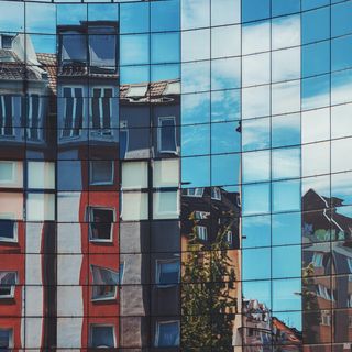 Eine Glasfassade, in der sich der Himmel und andere Gebäude spiegeln.
