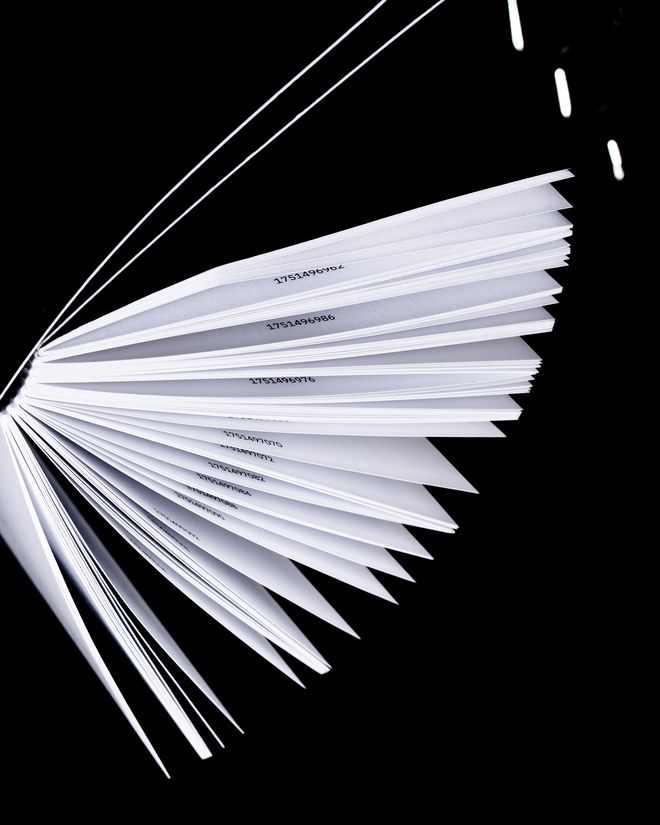 Nahaufnahme eines aufgefächerten Booklets, weiße Seitenkanten mit gedruckten Zahlen, schwarzer Hintergrund.