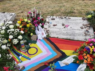 The photo shows various flower arrangements at the memorial stone for the homosexual men imprisoned and murdered by the Nazis in the Buchenwald and Mittelbau-Dora concentration camps. The memorial plaque bears the inscription (in German and English): »In memory of the homosexual men that suffered here / There were 650 Rosa Winkel prisoners in the Buchenwald concentration camp between 1937 – 1945. Many of them lost their lives«.