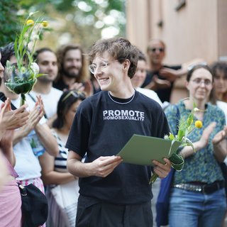 Felix Deiters mit Urkunde und Blumen lächelnd in einer Menschenmenge