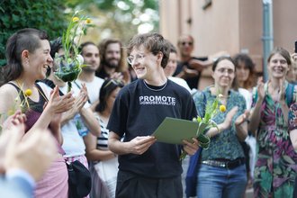 Felix Deiters mit Urkunde und Blumen lächelnd in einer Menschenmenge
