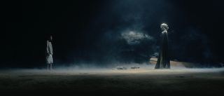 Film still from »DROWNING IS SILENT« by Alexander Knauer: in a dark, foggy scene, a boy faces a veiled figure. A rescue boat lies in the background.