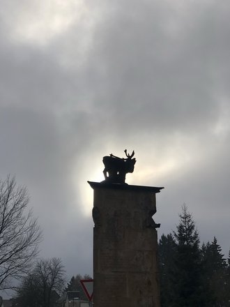 Aufnahme der Statue eines Hirsches im Abendlicht. Eine Shilouette ist erkennbar vor wolkigem Himmel.