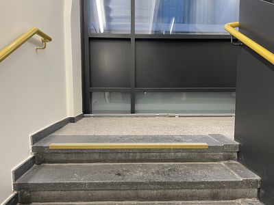 Im Treppenhaus der Coudraystraße 7 sind die Treppenstufen mit kontrastreich mit einem gelben Klebeband auf dunkler Trittstufe markiert.