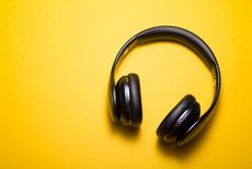 The photo shows headphones against a bright yellow background.