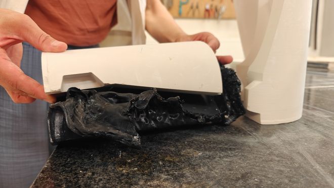 Eine Hand hebt den oberen Teil einer weißen Gießform an und gibt den Blick auf die schwarze PLA-Form im Inneren frei.