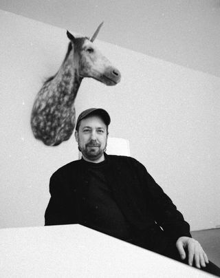 Porträt von Marcel Walldorf in einem Innenraum, hinter ihm hängt ein präparierter Einhornkopf an der Wand
