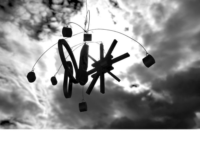 Ein Mobile von unten aufgenommen vor einem stark bewölkten Himmel, durch den die Sonne bricht