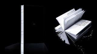 Book view against a black background: a black volume with exposed thread binding stands on the left, while an artist’s book is fanned open on the right, showing pages with variable letterforms.