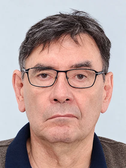Portrait of Achim Preiß wearing dark-framed glasses against a light background.