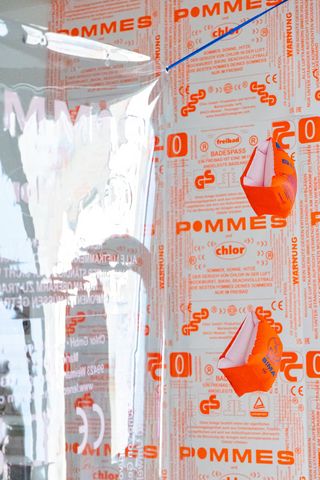 Abbildung des Plakates, das von der Decke hängt, daneben hängen Schwimmflügel für Kinder in Neon-Orange
