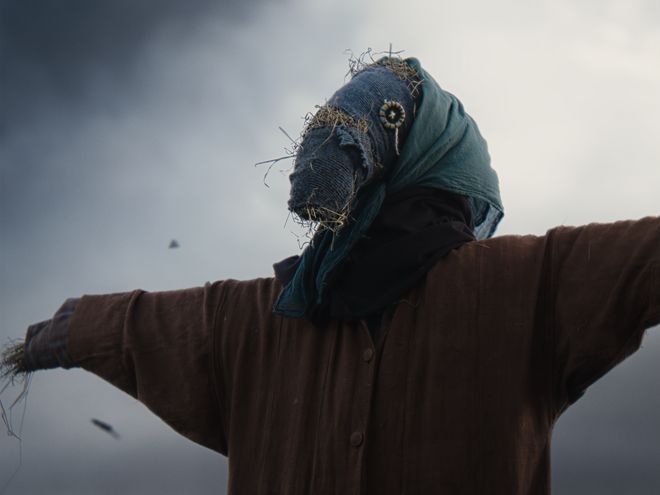 Vogelscheuche mit ausgebreiteten Armen auf einem Feld unter bewölktem Himmel.