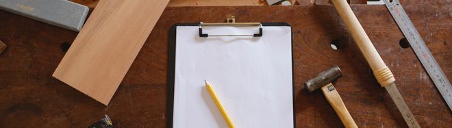 Klemmbrett, Bleistift, Hammer und Lineal auf einer Werkbank