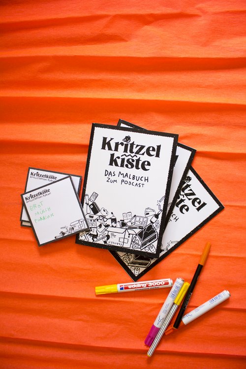 Foto des Kritzelkiste-Malbuchs mit ein paar daneben liegenden Stiften