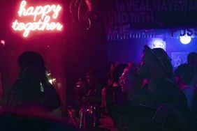 Personen in einer dunklen Bar, leuchtender Schriftzug "happy together"