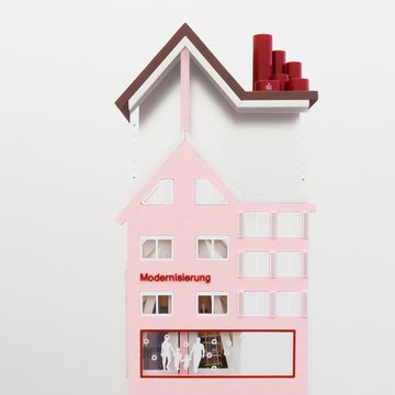 Model-like house object by Karla Zipfel in soft pink and white tones, featuring stylized windows and the word “Modernisation” on the façade.
