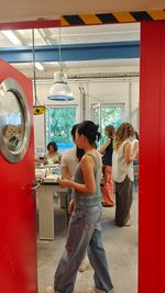 Isa Schreiber’s course focuses entirely on porcelain as a material. View through an open red door into the plaster and mould-making workshop. Several students work at benches with plaster moulds and models.