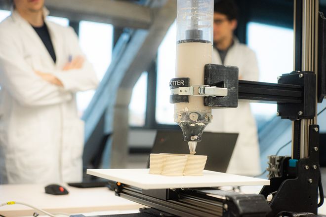 zwei Personen sehen dem 3D-Drucker bei der Arbeit zu