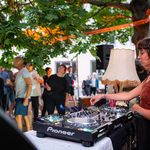 Tanzende Menschen und eine Frau am DJ-Pult